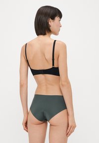 Svart bh med tunna justerbara band och bakknäppning; tillsammans med mörkgröna högmidjade bikiniunderdelar, slät textur, minimalistisk design.