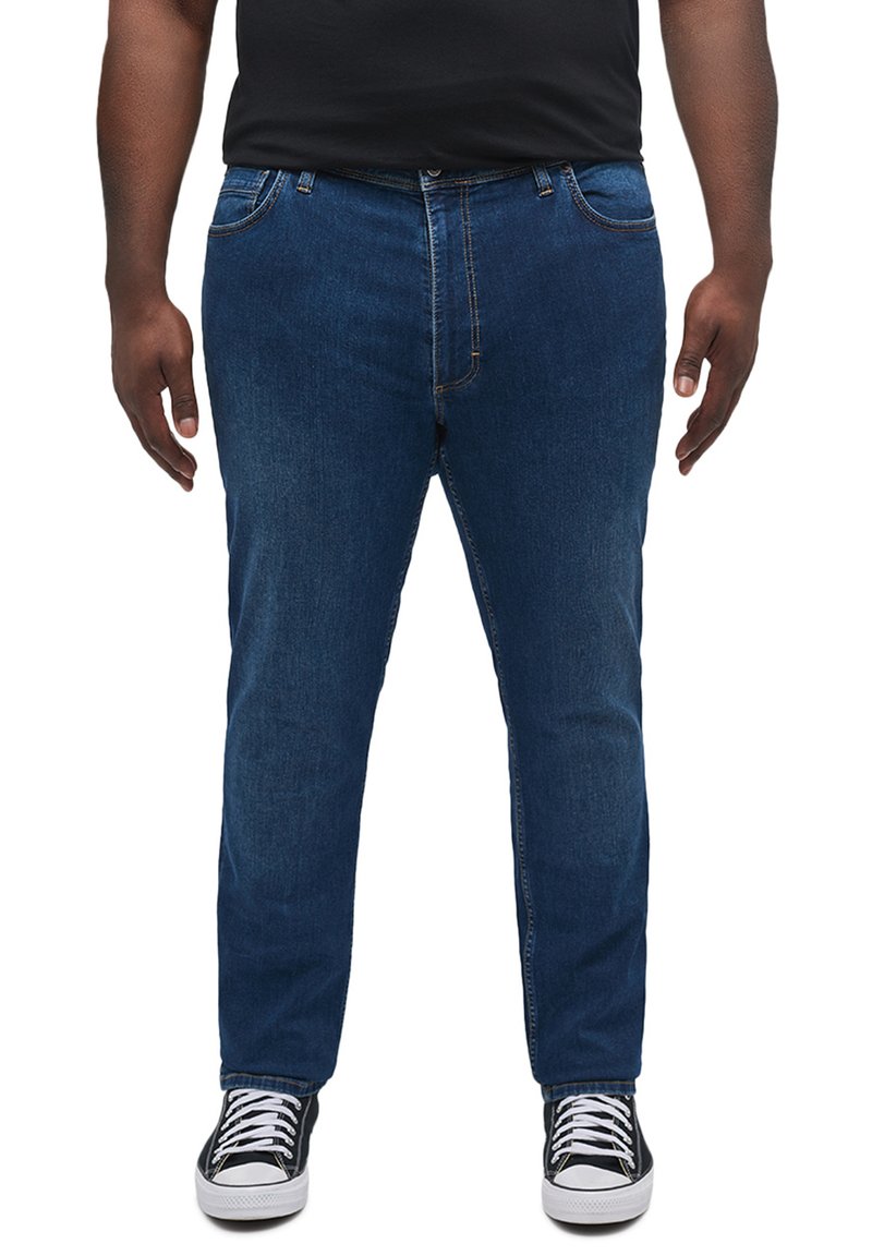 Jeans din denim albastru, cu croi drept, cinci buzunare, cusături vizibile și sistem de închidere cu nasture, asortați cu adidași negri și o cămașă neagră.