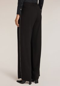 Brede zwarte broek met een gladde textuur, voorzien van een contrasterende zilveren zijstreep, elastische tailleband en een comfortabele pasvorm.