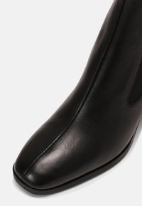 Primer plano de una bota de tobillo de cuero negro con punta cuadrada y costura que corre por el centro.