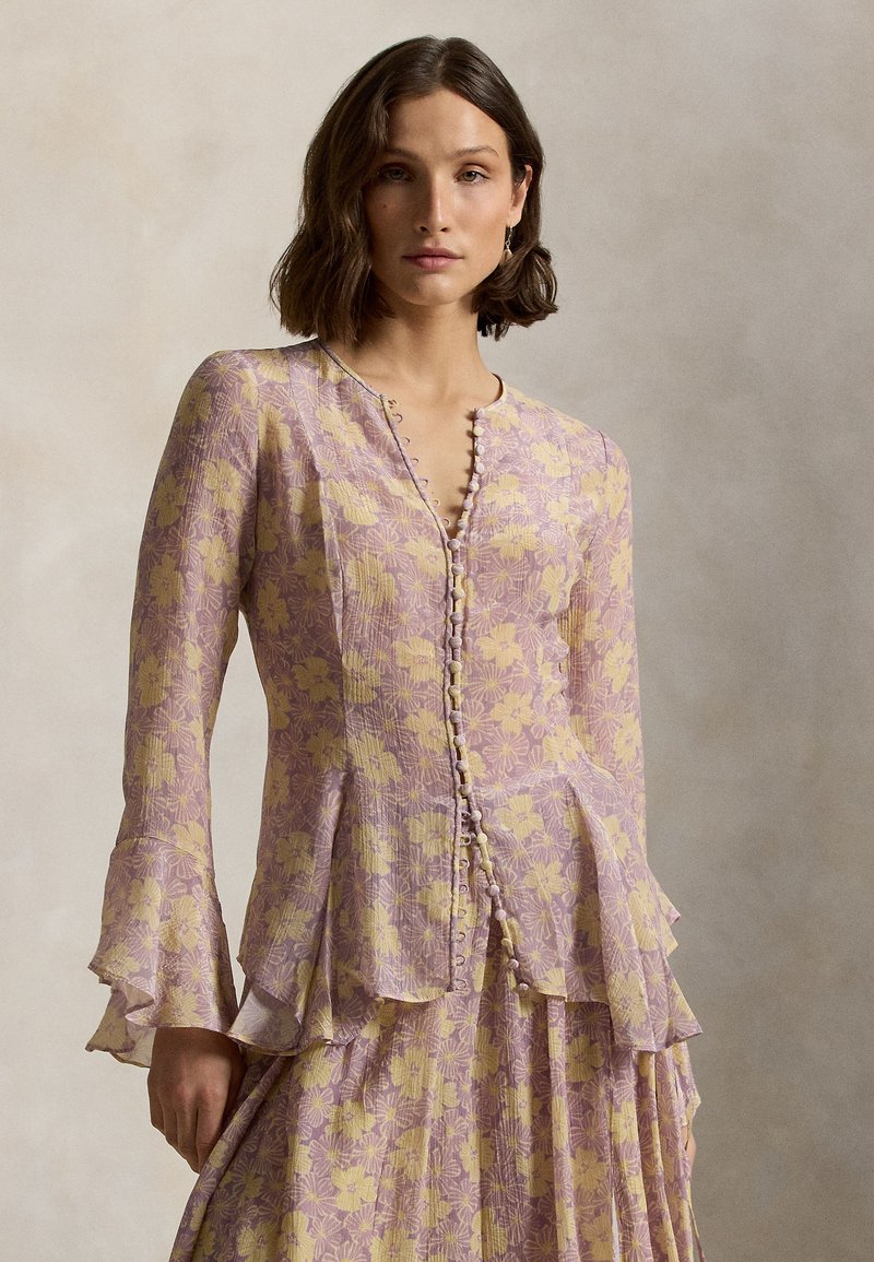 Bluse mit floralem Muster in zartem Lavendel und Gelb, mit langen Ärmeln, einem ausgestellten Saum und dekorativen Knöpfen auf der Vorderseite.