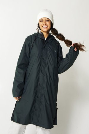 Cappotto impermeabile verde scuro con cappuccio, dotato di chiusure a bottoni, tasche laterali e corde regolabili. Berretto bianco indossato sulla testa.