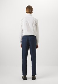 Bela srajca s kratkimi rokavi, v kombinaciji s temno modrimi hlačami, ki imajo ohlapno prileganje in žepi. Preprost dizajn, teksturirana tkanina.