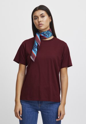 Bordeauxrood katoenen T-shirt met een ontspannen pasvorm, gecombineerd met een blauwe sjaal met bloemenpatroon en rode en blauwe strepen langs de randen.