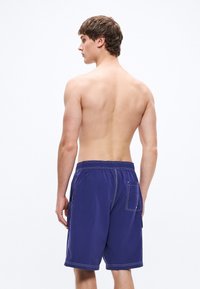 Ανδρικά μαγιό σορτς σε ναυτικό μπλε χρώμα, κατασκευασμένα από ελαφρύ ύφασμα, με ελαστική μέση, πλευρικές τσέπες και αντίθετες ραφές σε λευκό χρώμα.