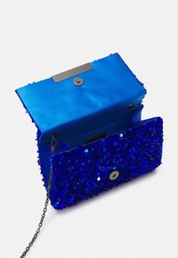 Kopertówka w kolorze królewskiego niebieskiego, zdobiona cekinami, z satynowym wnętrzem i srebrnym łańcuszkiem na ramię, otwarta, aby pokazać zapięcie na magnes i wewnętrzną kieszonkę.
