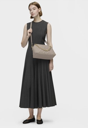 Sac à main beige avec un motif texturé, des accents de chaîne dorée et une base rectangulaire, associé à une robe sans manches grise foncée et des ballerines noires.
