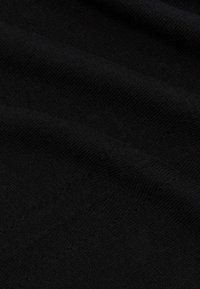 Musta kangas, jossa on teksturoitu neulospinta, esittelee sileitä taitoksia ja hienovaraisia vaihteluita pinnan syvyydessä.