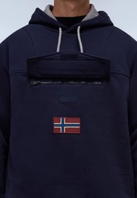 Sudadera azul marino con forro gris en la capucha, que presenta un bolsillo con cremallera y un parche bordado de la bandera noruega en el frente. Textura de tela suave.