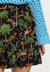 Gonna nera con stampa di foglie tropicali e palme nei colori verde, arancione e blu, con orlo arricciato e dettaglio in vita a fiocco. Top lavorato a maglia blu.