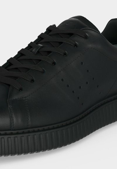 Μαύρο sneaker χαμηλού τύπου με διάτρητο σχέδιο στην πλευρά, επίπεδα κορδόνια και παχιά αυλακωτή σόλα, εμφανισμένο σε κοντινή γωνιακή άποψη.