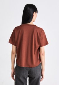 Roestkleurig t-shirt met korte mouwen, een relaxte pasvorm en een soepele textuur, gecombineerd met donkergrijze high-waisted jeans.