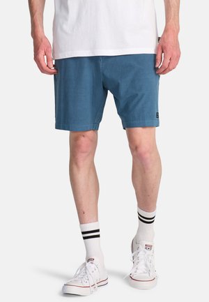 Pantaloncini blu in misto cotone, con taglio dritto e fronte piatto, abbinati a sneakers bianche e calzini a righe.