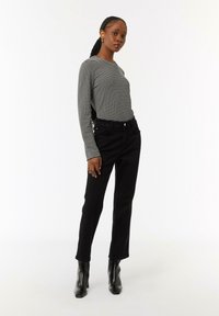 Gestreiftes Langarmshirt in Grau und Schwarz mit Rundhalsausschnitt, kombiniert mit schwarzen geraden Jeans und schwarzen Stiefeletten mit Absatz.