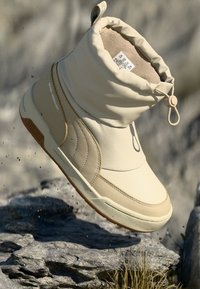 Beige waterdichte enkellaars met een gevoerde bovenkant, een glad synthetisch exterieur, rubberen zool en een trekkoordsluiting voor een verstelbare pasvorm.