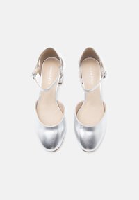 Ασημί μεταλλικές σανδάλες με τακούνι, στρογγυλή μύτη και ρυθμιζόμενη θηλιά στον αστράγαλο. Λείο υλικό, μινιμαλιστικός σχεδιασμός και επίπεδο τακούνι.