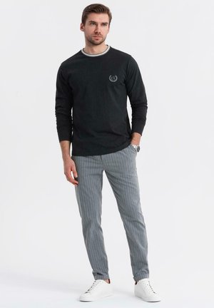 Camisa negra de manga larga con cuello redondo gris claro, combinada con pantalones a rayas grises y zapatillas blancas. Ajuste casual, con un branding mínimo.