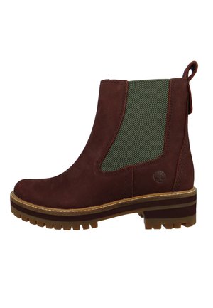 Brązowy zamszowy botek Chelsea z zieloną elastyczną wstawką po bokach, pętelką na pięcie, grubą podeszwą typu lug oraz wytłoczonym logo Timberland w pobliżu podeszwy.