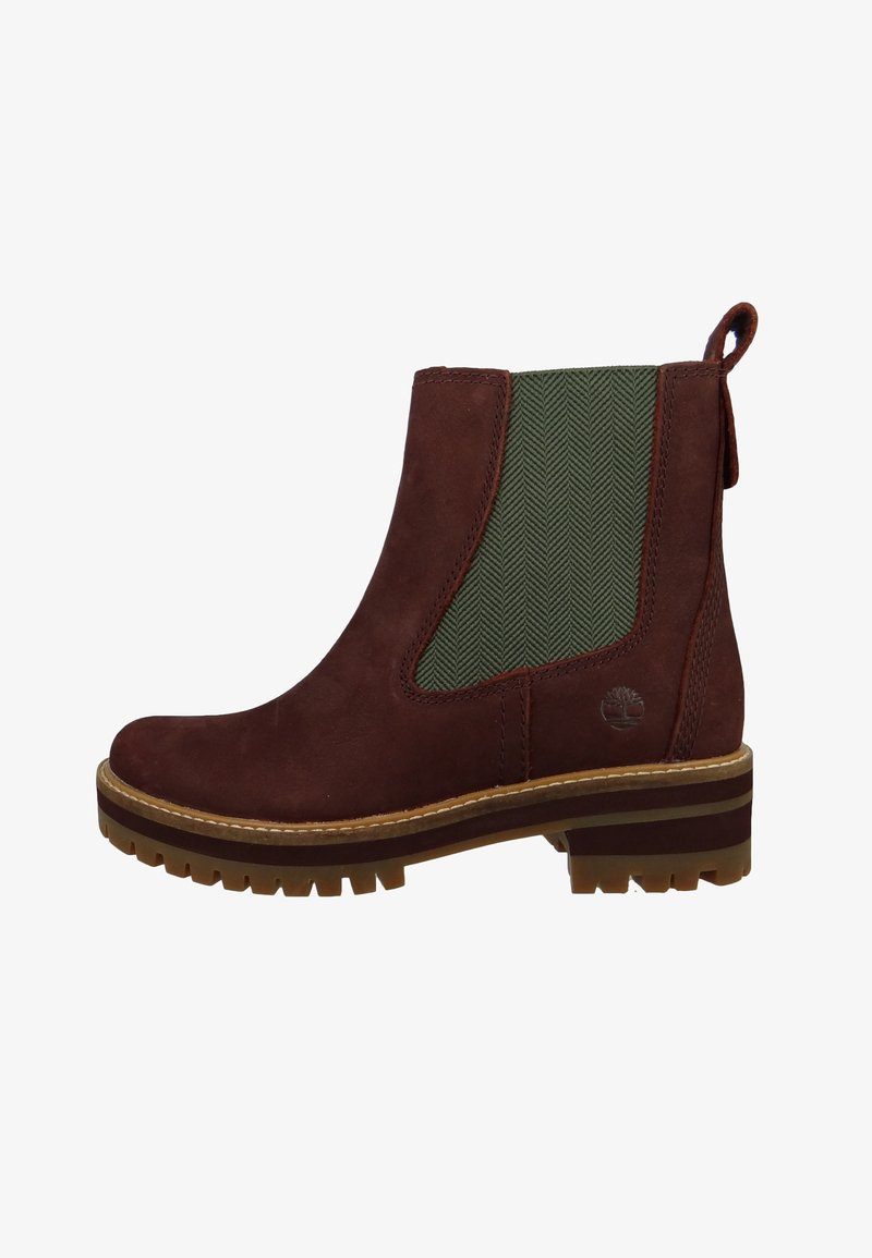 Bottine Chelsea en daim marron avec panneau élastique vert sur le côté, languette de traction au talon, semelle épaisse à crampons, et logo Timberland embossé près de la semelle.