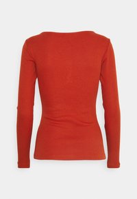 Långärmad topp i en solid bränd orangefärg, med en figurnära design, ribbad textur och en grund rundad halsringning.