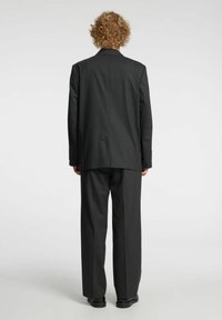 Czarny garnitur z dopasowaną marynarką z pojedynczym rozcięciem i spodniami o szerokich nogawkach, oba wykonane z gładkiej tkaniny, widoczne od tyłu.