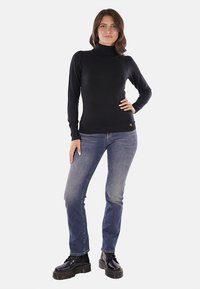 Maglione nero a collo alto in maglia con polsini e orlo a costine, abbinato a jeans in denim blu e stivali neri con lacci, con un sottile accento del logo.