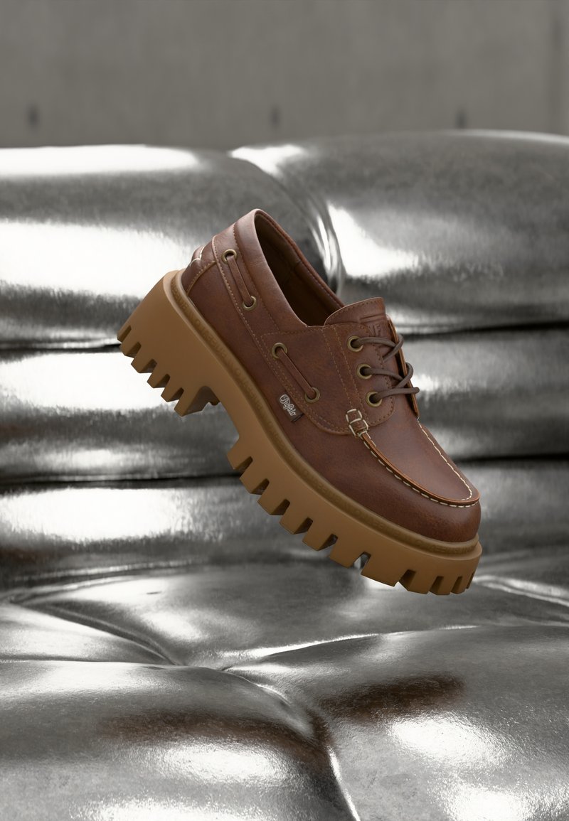Καφέ δερμάτινο παπούτσι με κορδόνια και χοντρή, ανθεκτική ταμπά σόλα που αιωρείται πάνω από μια λαμπερή ασημί μαξιλαρωτή δερμάτινη επιφάνεια.