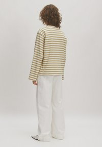 Gestreepte lange mouwen shirt in crème en lichtbruin, gecombineerd met losse witte broek. Zachte stof, ronde halslijn en ontspannen pasvorm.