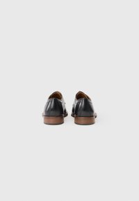 Chaussures habillées en cuir noir avec une finition lisse, forme arrondie et talons empilés marron. Présentent des coutures minimales et un design classique.