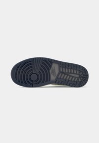 Semelle d'une basket Nike de couleur foncée montrant des motifs de semelle circulaires et rectangulaires avec le logo Nike au milieu du pied.