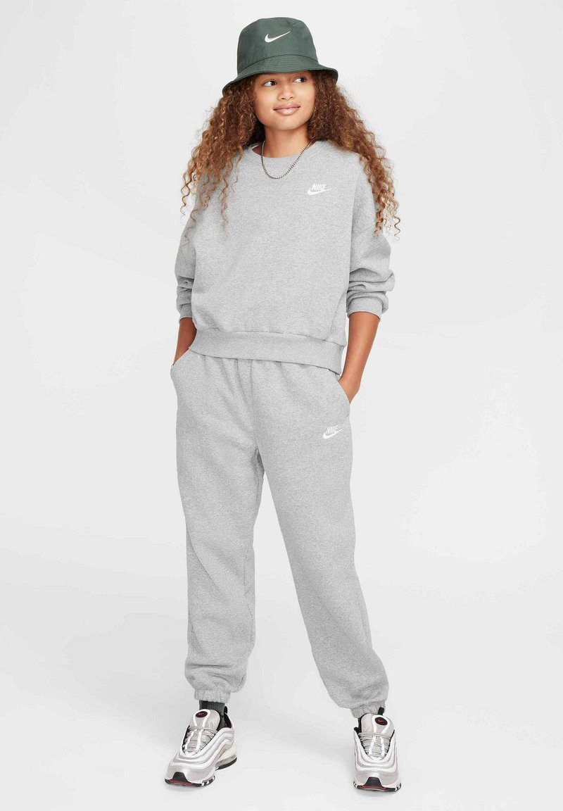 Szary sweatshirt i dresy z białym logo Nike, zestawione z zieloną czapką typu bucket i srebrnymi butami sportowymi z czarnymi akcentami.