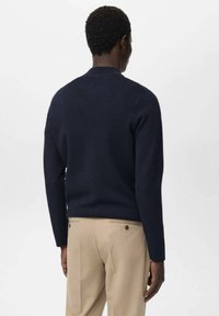 Suéter azul marino de material suave con cuello redondo y mangas largas, combinado con pantalones beige. Diseño minimalista, sin patrones visibles.