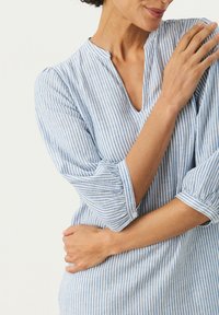 Chemise rayée bleue et blanche avec un décolleté, des manches trois-quarts et une coupe décontractée. Le tissu semble léger et texturé.