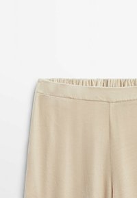 Beiga sammetbyxor med elastisk midja, som visar den övre framsidan och den släta tygtexturen.
