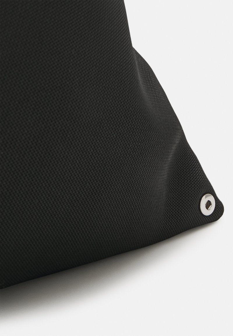 Cojín negro texturizado con forma triangular, que presenta un acento de ojal metálico en una esquina.