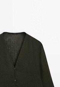 Chemise en lin vert foncé avec un col en V, des manches longues et deux boutons à l'avant. Le tissu a une finition texturée, ajoutant de la profondeur au design.