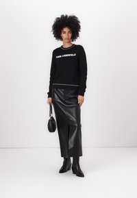 Melnas džemperis ar "KARL LAGERFELD" logotipu, apvienots ar melnu ādas svārku ar augstu jostasvietu, kuram ir priekšēja šķeltne. Gludas tekstūras, piegulošs dizains.