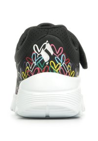 Schwarzer Sneaker mit einer strukturierten Oberseite, weißer Sohle und bunten Herzmustern an der Ferse. Verfügt über einen Klettverschluss.