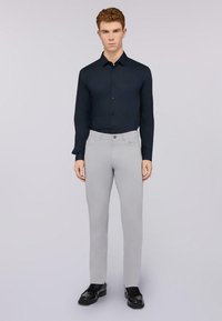 Camicia blu navy con bottoni, pantaloni grigi chiari aderenti e scarpe nere. La camicia ha un colletto e maniche lunghe, mentre i pantaloni presentano un taglio classico.