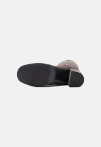 Γκρι μποτάκι αστραγάλου από σουέντ με αιχμηρή φτέρνα, λεία μαύρη σόλα από καουτσούκ και ελάχιστες ραφές. Διαθέτει στρογγυλεμένη σχεδίαση μύτης.