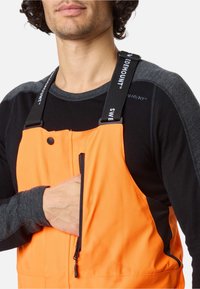 Oranje geïsoleerde overall met zwarte accenten. Voorzien van verstelbare banden, een ritszak en zachte stof. Geschikt voor buitenactiviteiten.