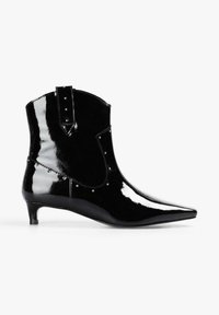 Botines de charol negro con punta puntiaguda, tacón bajo tipo kitten y tachuelas decorativas a lo largo del lateral y la silueta superior.