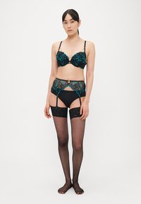 Črno spodnje perilo z turkizno cvetlično čipko; vključuje nedrček, pas za nogavice in ujemajoče se črne nogavice do stegen. Gladek tekstura.