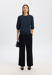 Granatowy pulower z krótkimi bufkami, zestawiony z wysokim stanem czarnych luźnych spodni o szerokich nogawkach oraz czarnymi szpiczastymi szpilkami. Akcesorium: mała czarna torebka.