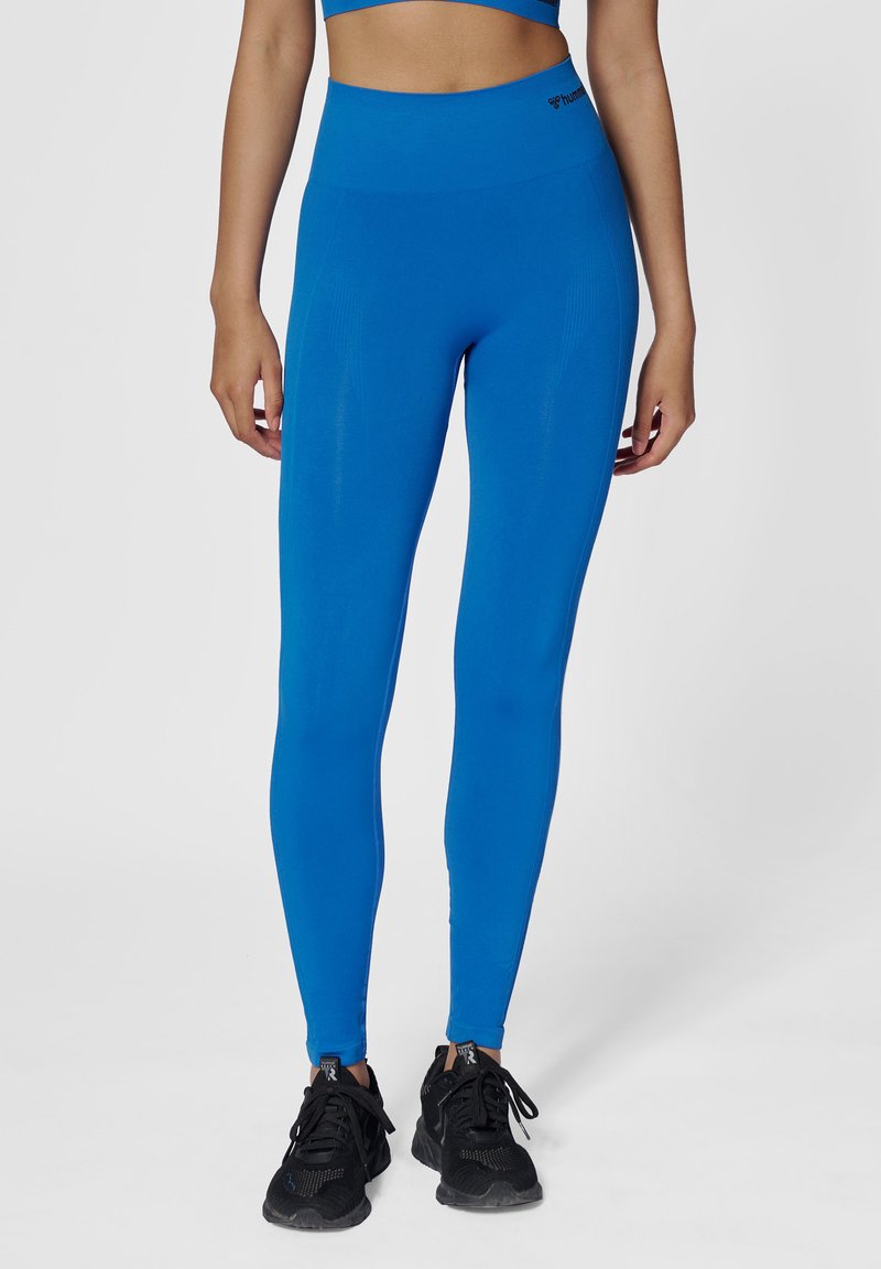 Blå högmidjade leggings gjorda av stretchtyg, med en mjuk textur och en åtsittande design, kombinerat med svarta träningsskor.