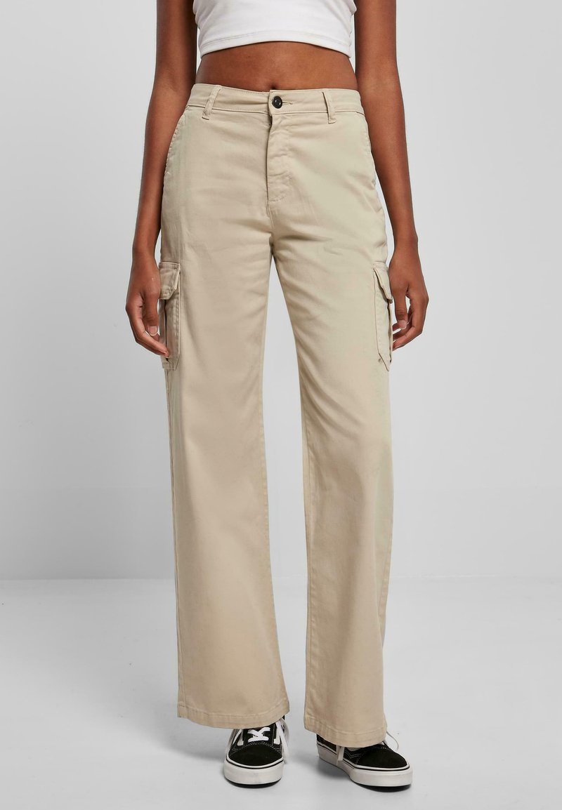 Pantalones cargo beige con un diseño de pierna recta, hechos de tela de algodón. Presenta dos bolsillos laterales y un cierre de botón en la cintura, combinados con zapatillas negras.