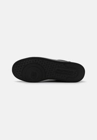 Black rubber shoe sole featuring a textured pattern with a circular logo in the center and a triangle tread design for traction.