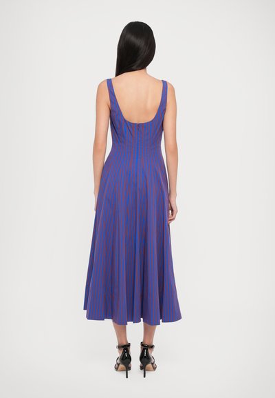 Blue and red striped sleeveless dress with a low back, flaring skirt, and lightweight fabric, paired with black sandals.