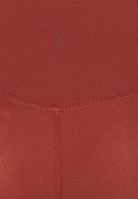 Haut de sport Nike en tissu rouge uni. Il présente un design sans couture avec des coutures décoratives et un accent de logo subtil qui se fond avec la couleur.