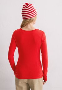 Rotes Langarmshirt mit rundem Halsausschnitt, aus glattem Stoff gefertigt, kombiniert mit einer rot-weißen gestreiften Mütze.